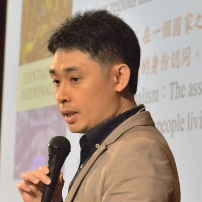 Dr. Brian C.H. Fong speaks on stage, holding a microphone, in front of a presentation.