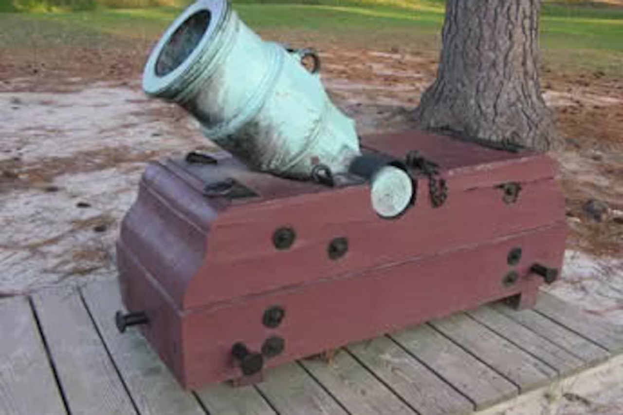 A mortar is on display in a grassy field with several trees in the distance.