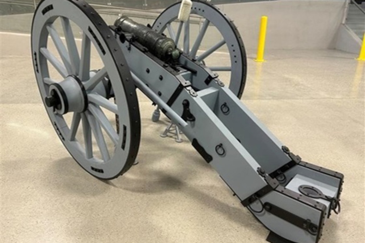 A cannon mounted on a gray two-wheeled vehicle is on display in a large room.