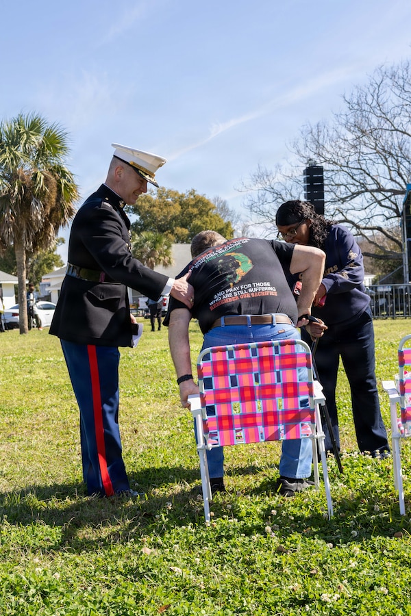 U.S. Marine Corps Col. Michael Brennan, chief of staff, Marine Forces Reserve, and Ms. Beverly Boyd, director of protocol, assist Samuel Manzella, a retired U.S. Marine Corps veteran at the Algiers Mardi Gras Festival in New Orleans, Feb. 28, 2026. The Algiers Point neighborhood in New Orleans has served as the headquarters of MFR since 2011. The Algiers Mardi Gras Festival is a celebration designed to unite diverse organizations and foster a strong sense of community. (U.S. Marine Corps photo by Lance Cpl. Edward Spears)