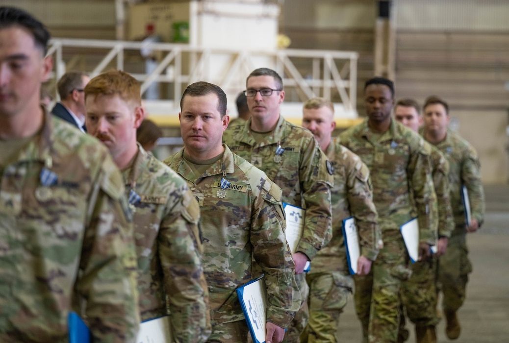 Members of the 5-5 Air Defense Artillery Battalion, assigned to Fort Sill, walk back to their seats after being awarded the Air and Space Achievement Medal at Altus Air Force Base, Oklahoma, March 4, 2026. From weight distribution and tie-down configurations to communication protocols, every step is critical in the process of executing proper loading procedures for Army combat vehicles onto the C-17 Globemaster III aircraft. (U.S. Air Force photo by Airman 1st Class Emma Wright)