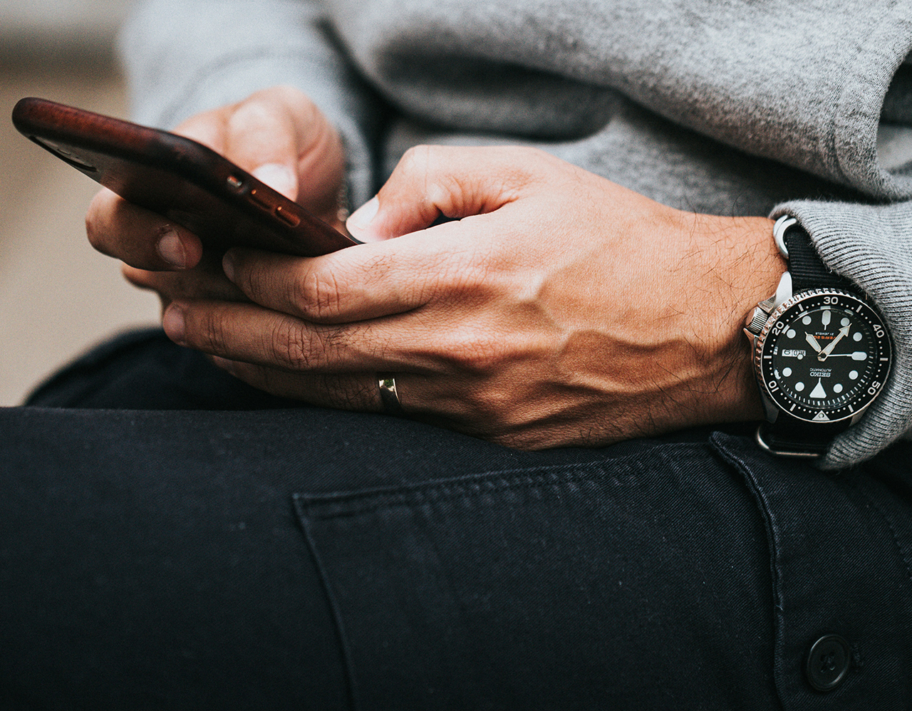 Person in gray sweater wearing black and silver chronograph watch, typing on a phone.