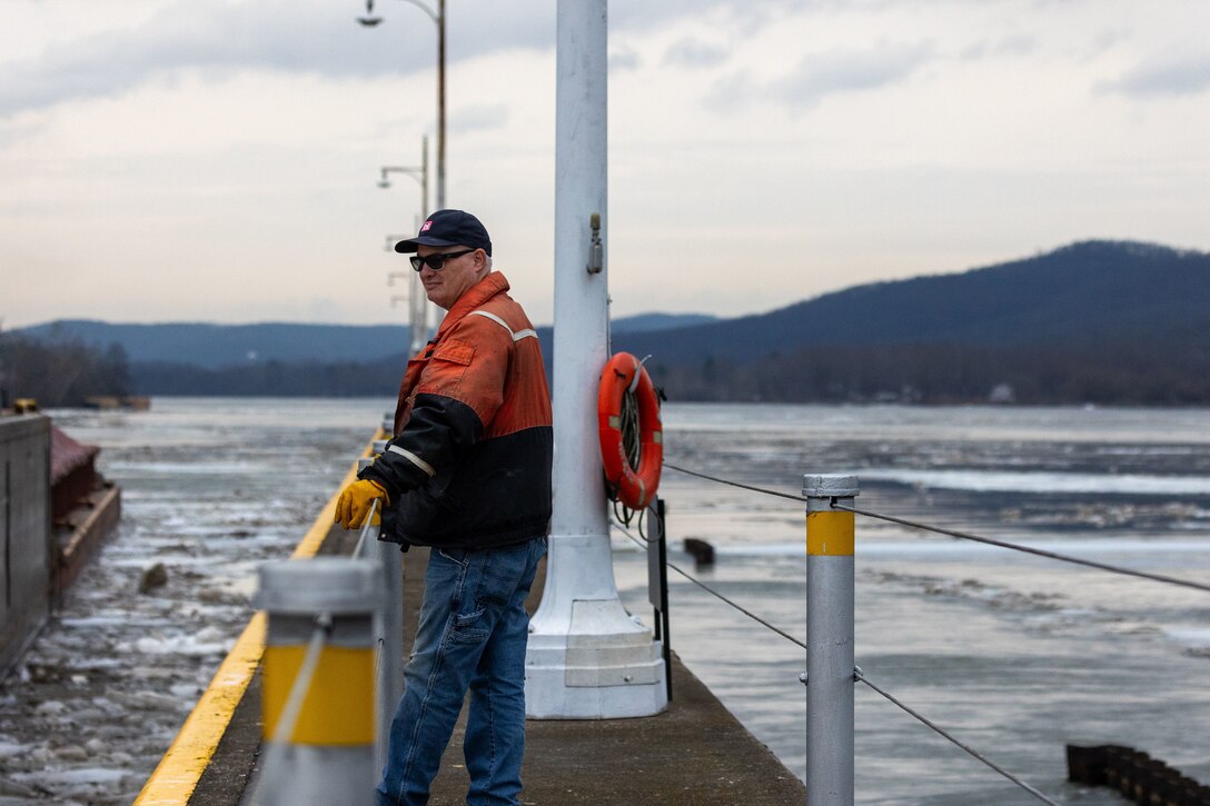 A man stands on a concrete wall in front of a river during winter.