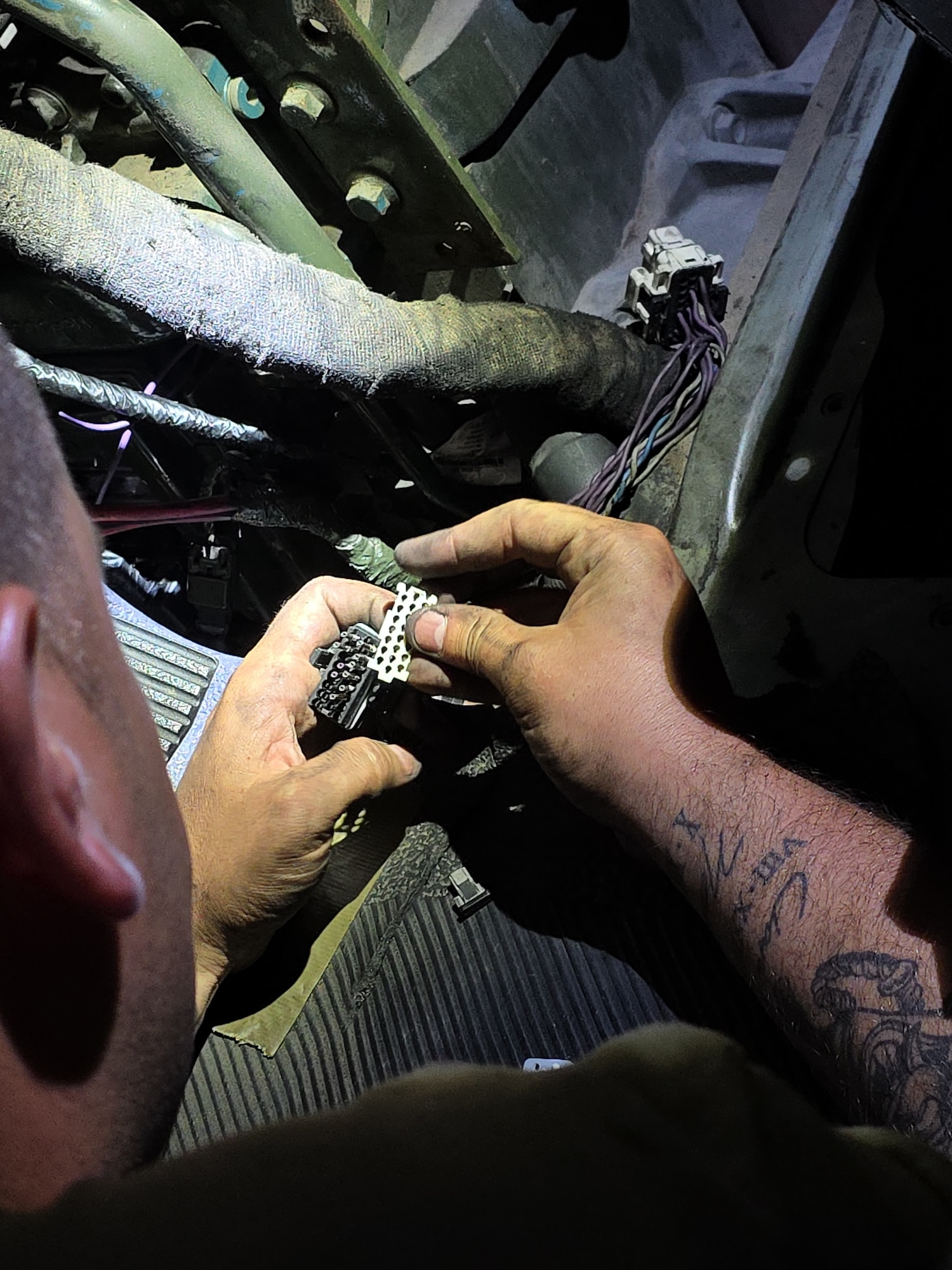 A photo of a man working on a vehicle. He seems to be unplugging something electrical.