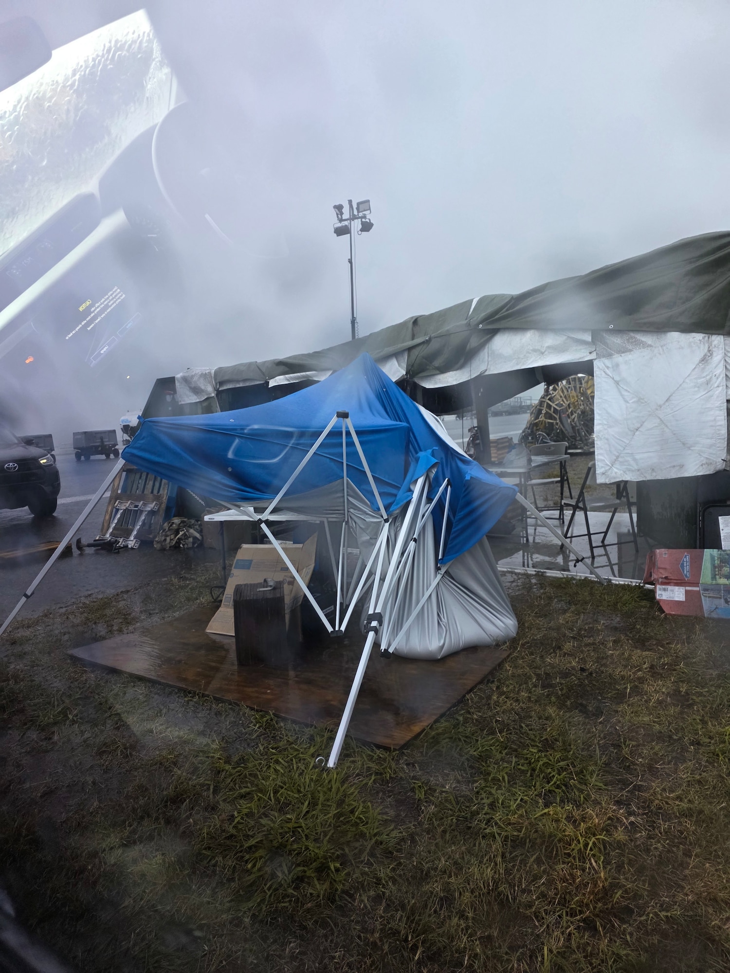 A photo taken inside a vehicle of a bright blue canopy that is destroyed due to inclement weather. Rain distorts the image.