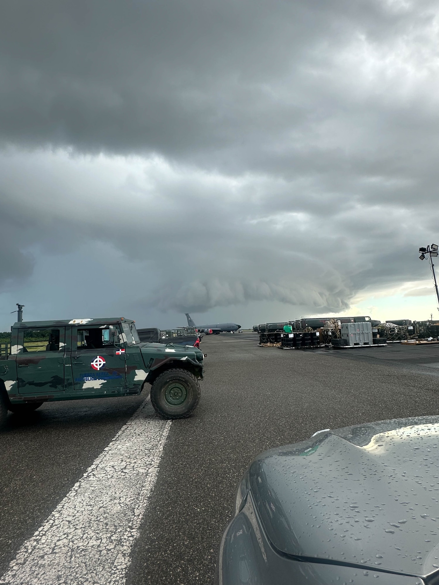 A photo form a vehicle, of a flightline and vehicles scattered throughout. There is a heavy storm coming towards the individual who is taking the photo. The skies are grey with a little bit of light at the end.