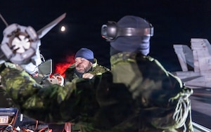Two Canadian service members stand next to an aircraft wing tip preparing it for takeoff.