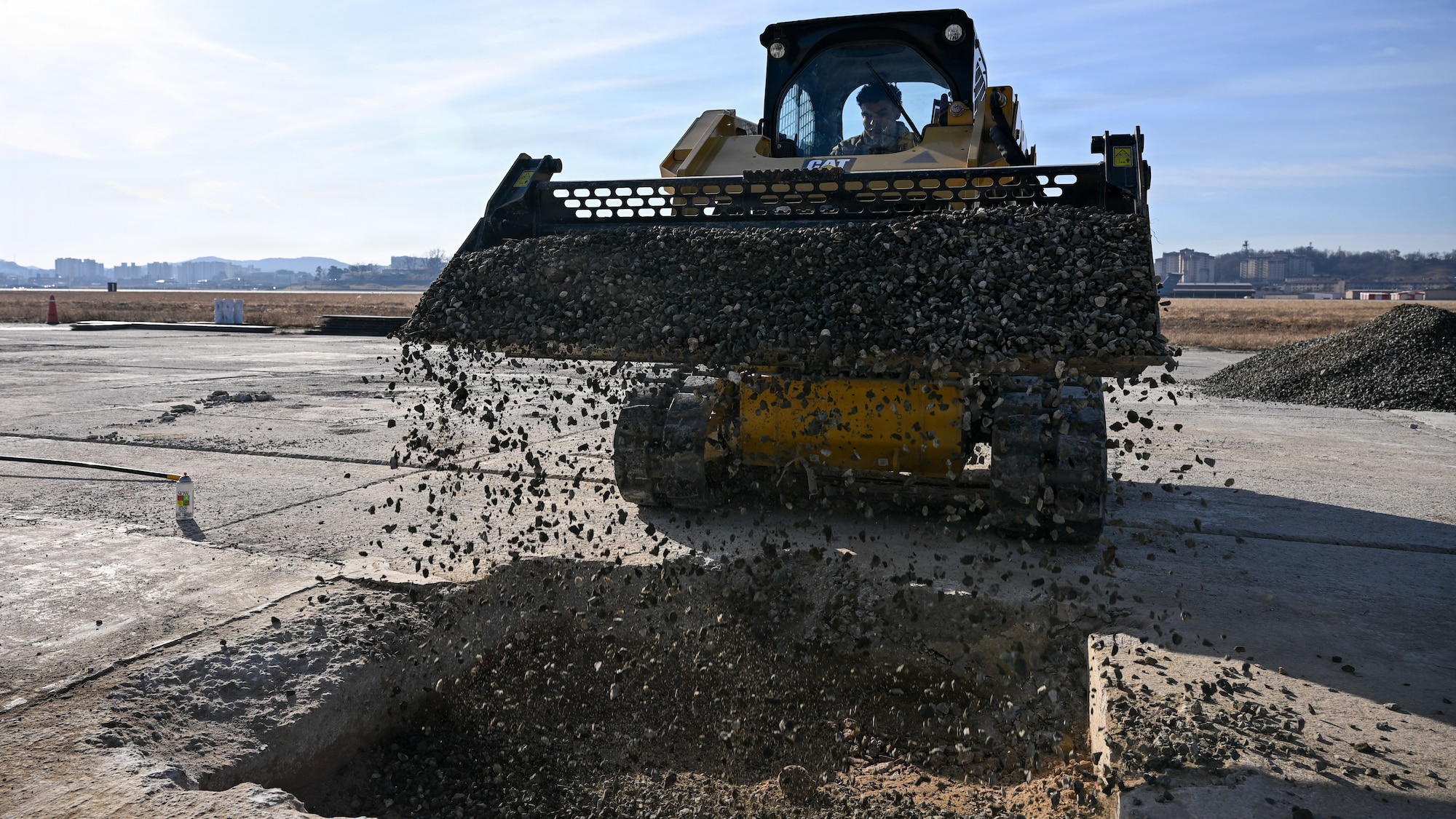 A U.S. Air Force Airman, assigned to the 51st Civil Engineer Squadron, dumps rocks into a crater during Rapid Osan Airfield Recovery training at Osan Air Base, Republic of Korea, Feb. 26, 2026. Airmen placed flowable fill concrete over compacted crushed stone as part of Osan’s ROAR concept, designed to rapidly generate aircraft launch capability. (U.S. Air Force photo by Senior Airman Rome Bowermaster)
