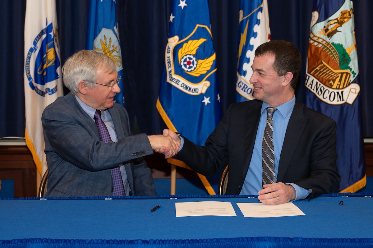 Image of two men shaking hands in front of flags.