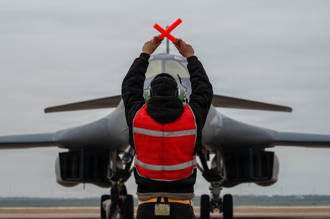 A U.S. Air Force B-1B Lancer crew chief marshals a B-1 after returning from a CONUS-to-CONUS mission in support of Operation Epic Fury, March 4, 2026. The B-1B is a long-range, multi-role bomber that carries the largest payload of precision guided and unguided munitions in the Air Force inventory. (U.S. Air Force photo)