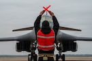 A U.S. Air Force B-1B Lancer crew chief marshals a B-1 after returning from a CONUS-to-CONUS mission in support of Operation Epic Fury, March 4, 2026. The B-1B is a long-range, multi-role bomber that carries the largest payload of precision guided and unguided munitions in the Air Force inventory. (U.S. Air Force photo)