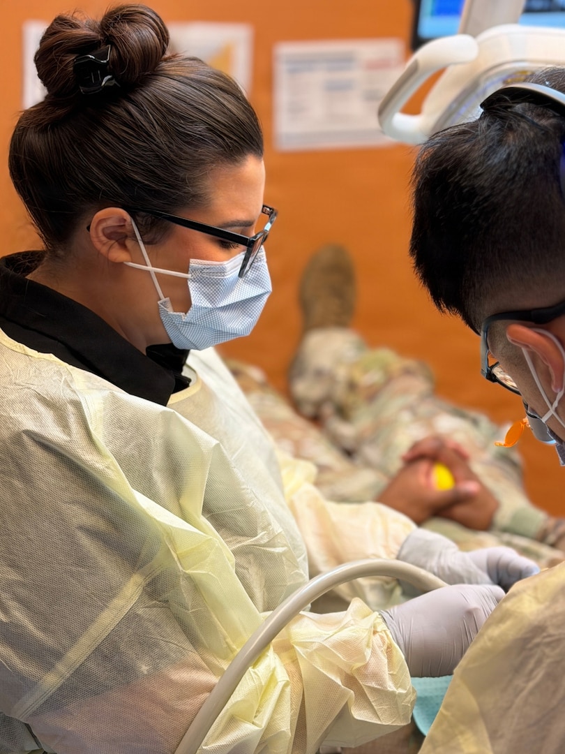 Dentist and Dental Assistant dressed in protective gear performs a procedure on a patient.