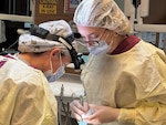 Dentist and Dental Assistant dressed in protective gear performs a procedure on a patient.