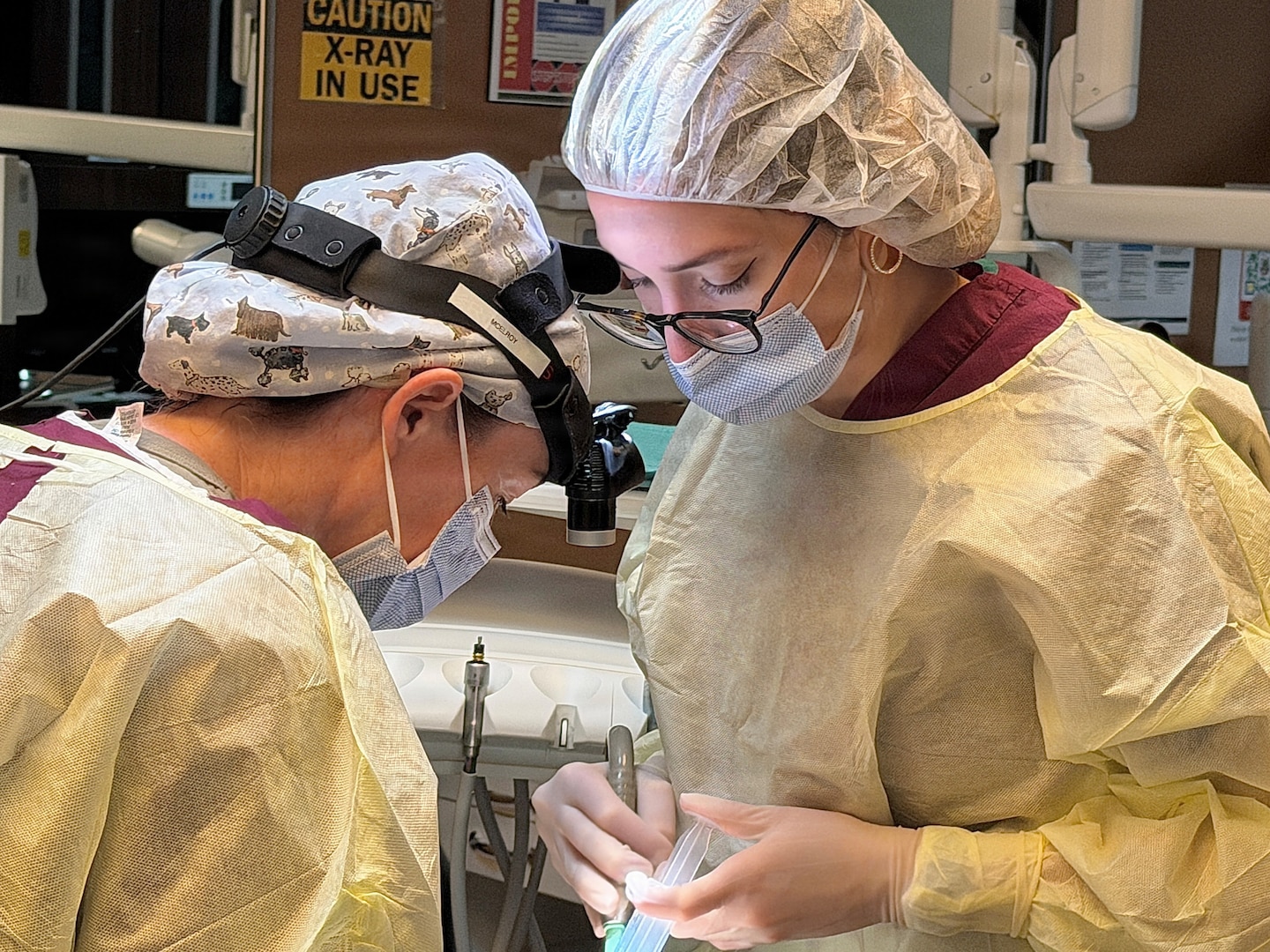 Dentist and Dental Assistant dressed in protective gear performs a procedure on a patient.