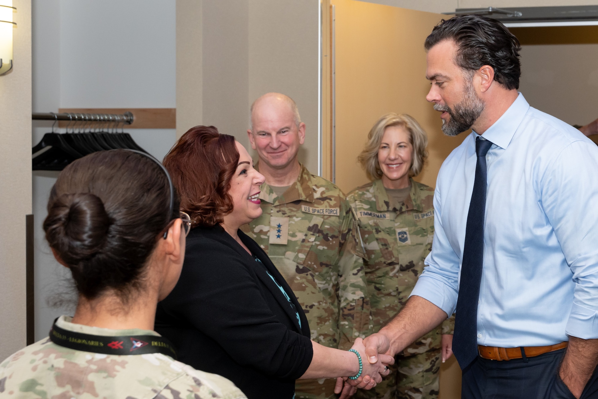 A female civilian shakes hands with a male civilian as military members look on