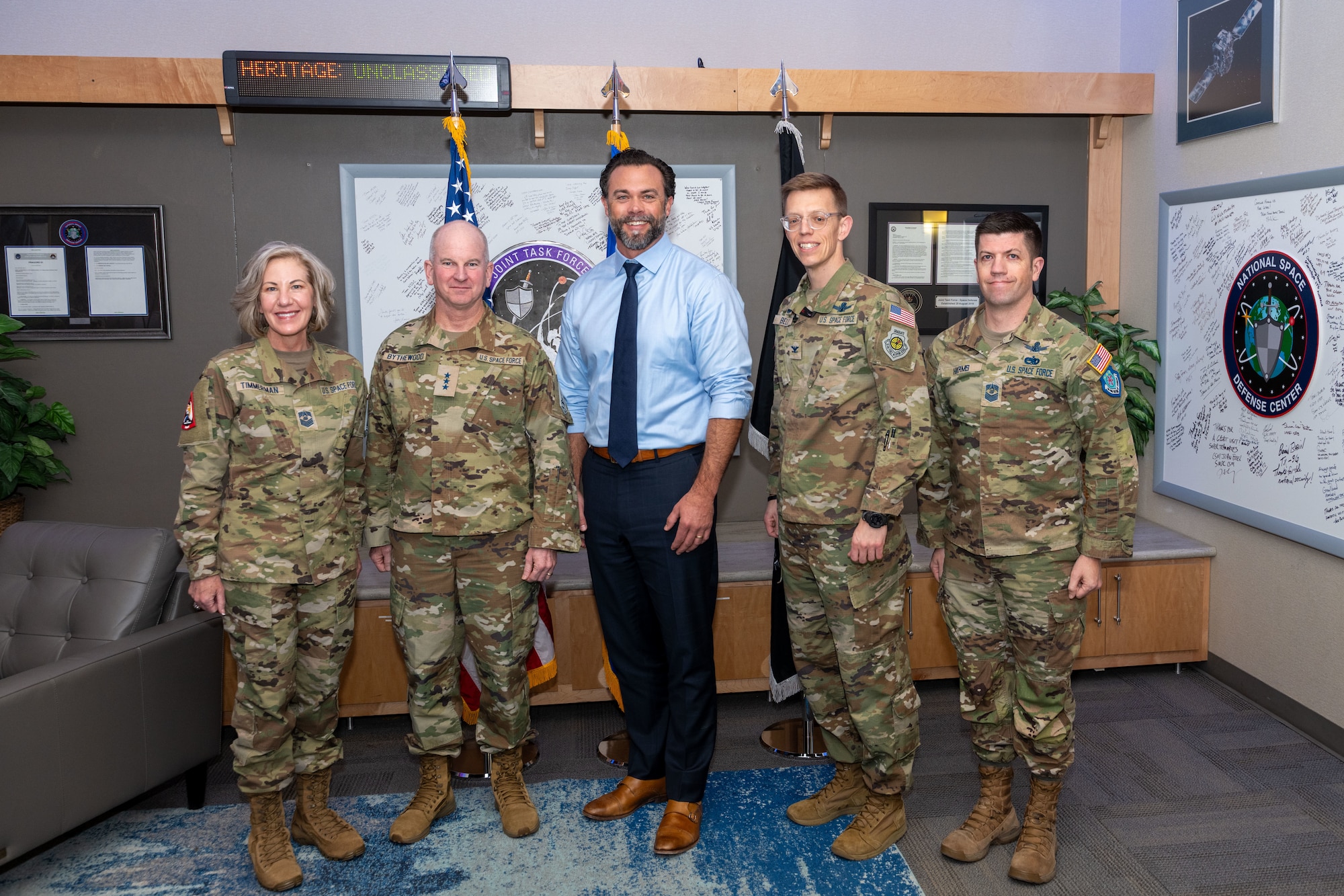 Four military members pose with a civilian in a unit heritage room