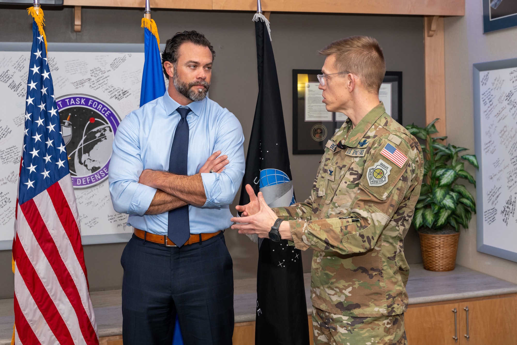 Military man talks to civilian man who listens with his arms crossed