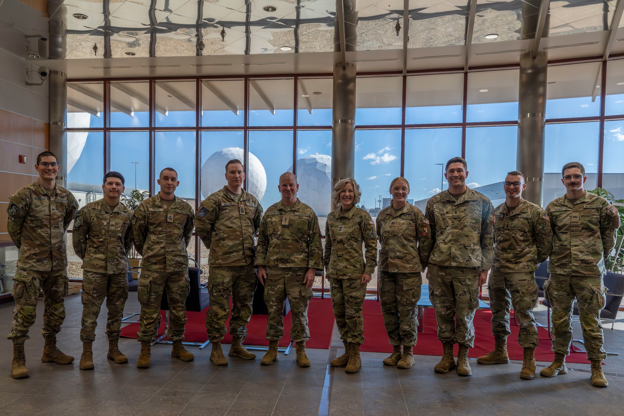 Ten military members pose for a picture in front of a window with a view of two giant space sensors