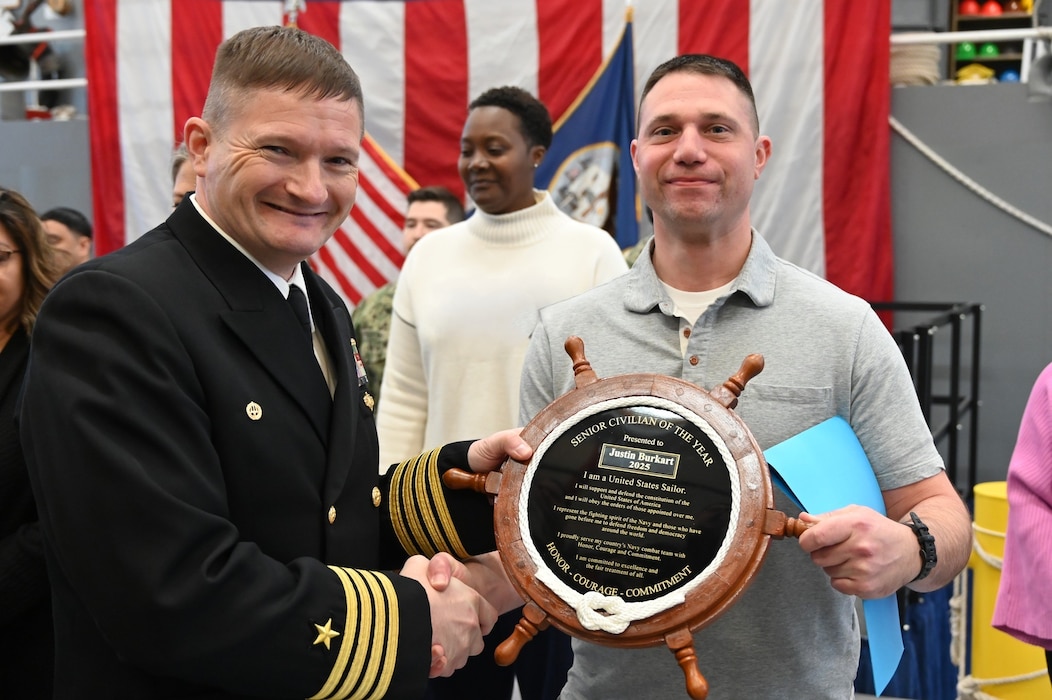 GREAT LAKES, Ill. (Feb. 26, 2026) Justin Burkart, a technical instructor at Surface Combat Systems Training Command (SCSTC) Great Lakes (GL), receives his Civilian of the Year award from Capt. Chris May, SCSTC GL’s commanding officer. (U.S. Navy photo by Kelsey Danner)