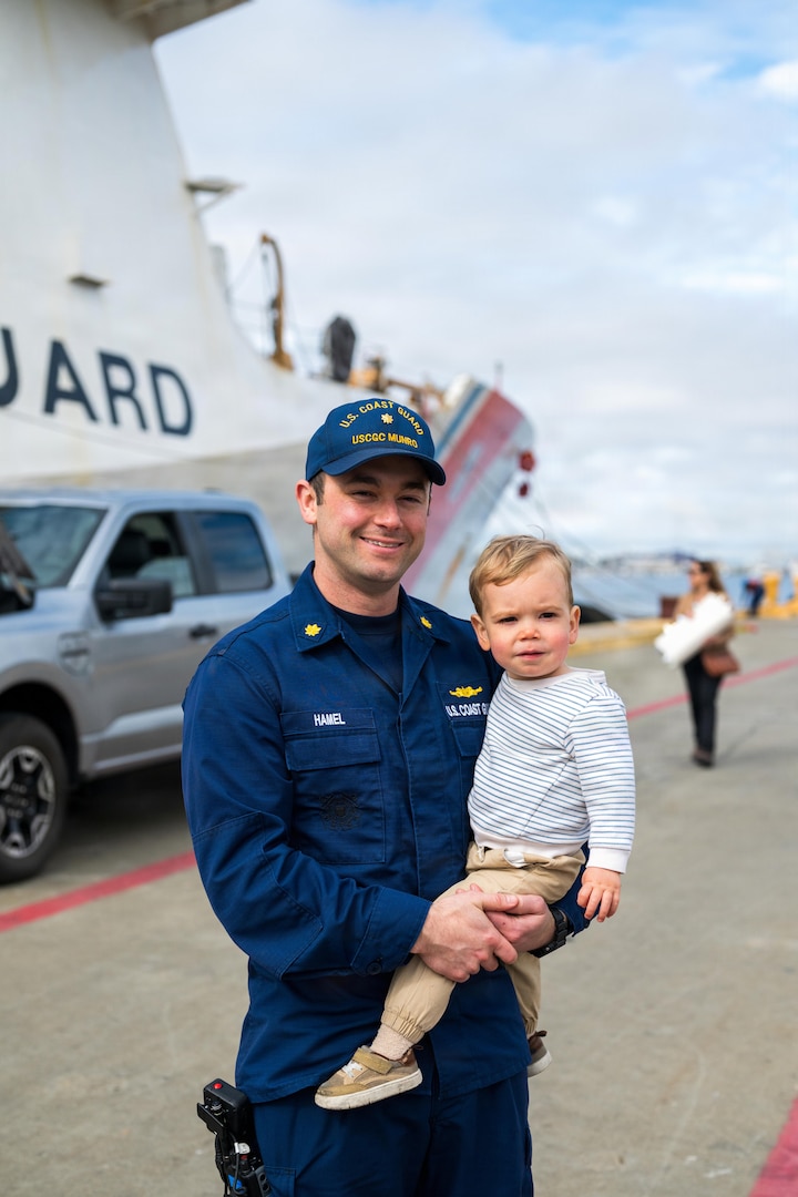 Lt. Cmdr. John Hamel, a crew member aboard the USCGC Munro (WMSL 755), holds his son after being greeted by family members during the cutter’s return to home port in Alameda, California, March 1, 2026. Munro is one of four U.S. Coast Guard Legend-class National Security Cutters homeported in Alameda.  (U.S. Coast Guard photo by Petty Officer 3rd Class Austin Wiley)