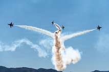 Five Thunderbirds aircraft split off in the sky, performing their "Low Bomb Burst" maneuver with mountains peaking from the bottom.