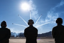 Five Thunderbird aircraft split off in the air with three Airmen silhouettes look on.