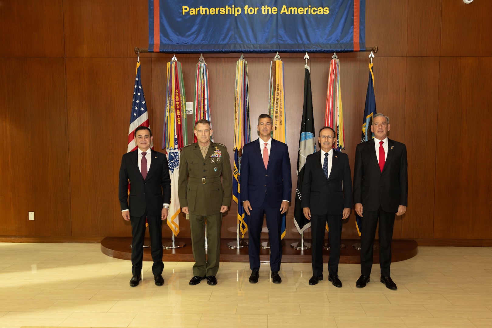 A man in a brown military uniform and a man in a dark blue suit pose for a photo in front of flags.