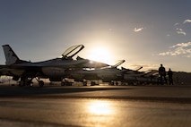 Thunderbird aircraft are lined up on the flightline with the Airmen standing on the right side of the photo.