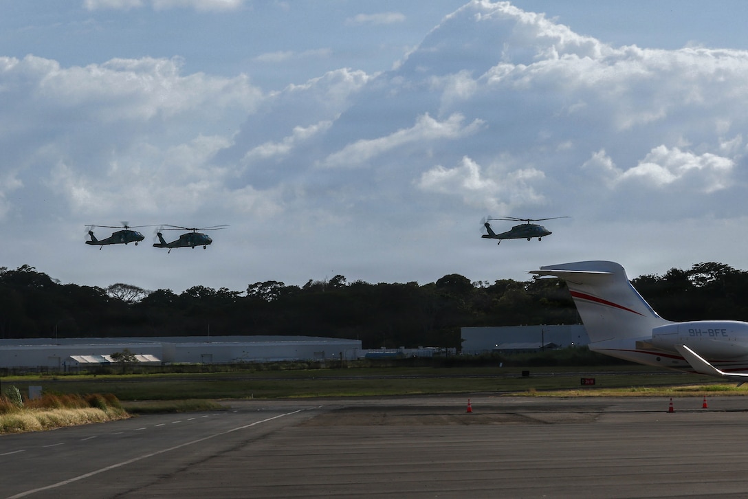 3 Military helicopters fly in the sky above an airfield.
