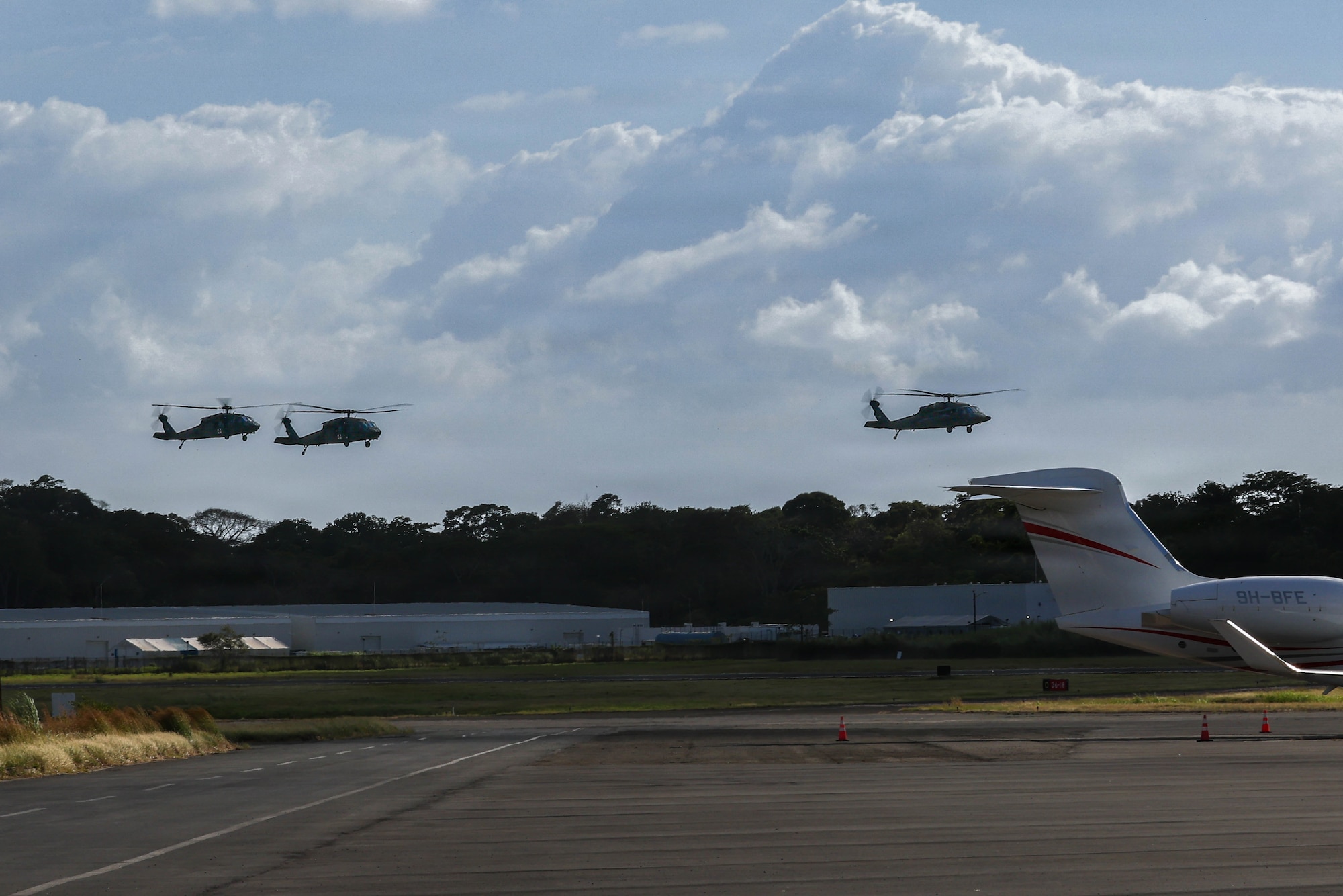3 Military helicopters fly in the sky above an airfield.