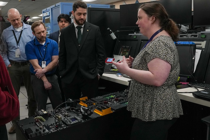 a woman addresses a group of people while standing in front of a software testing bench