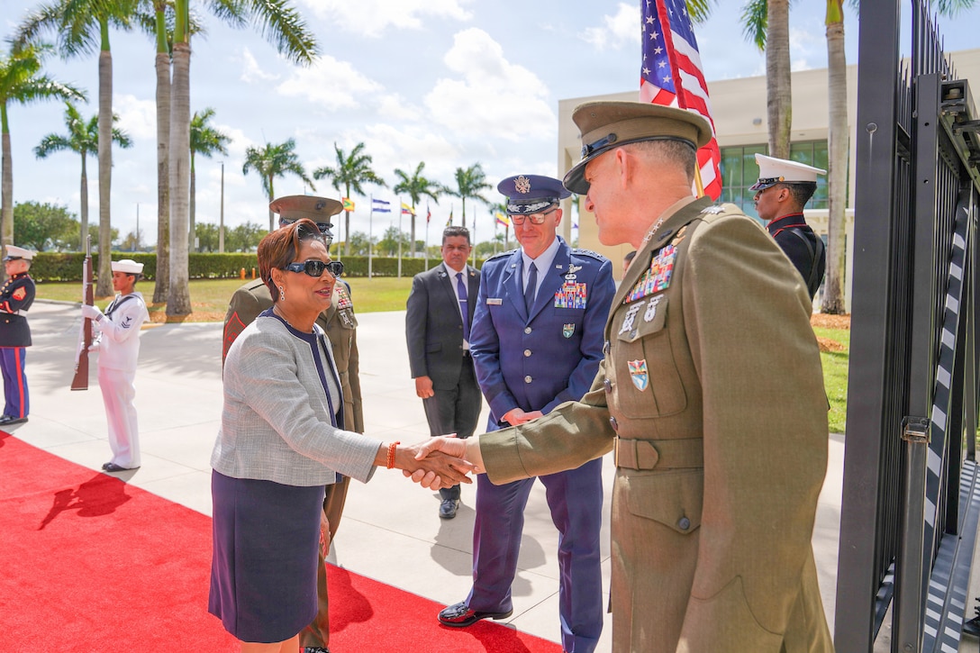 A woman in a white and blue dress shakes hands \with a man in a brown military uniform.