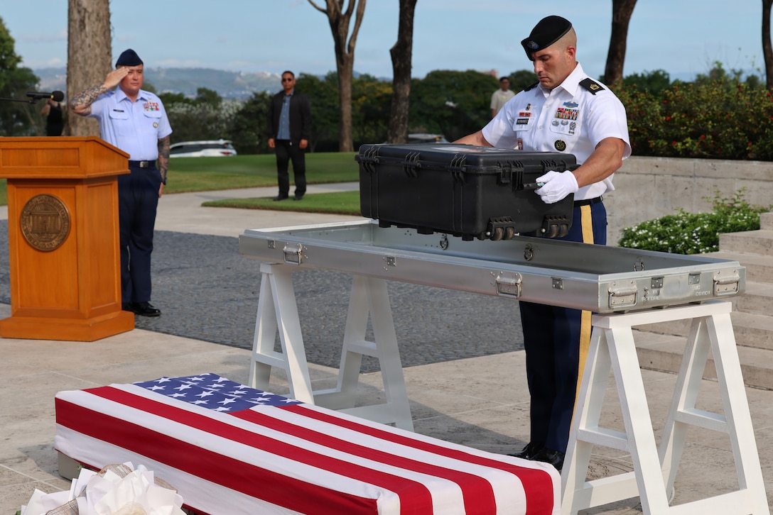 U.S. Army Sgt. 1st Class Nicholas Hernandez, Defense POW/MA Accounting Agency team sergeant, places the remains of the 100th U.S. Unknown DPAA disinterred during fiscal year 2026 while U.S. Air Force Tech. Sgt. Michael Castro, DPAA Operations Law noncommissioned officer-in-charge, and master of ceremony, renders a salute during the first-ever Repatriation Ceremony held at the Manila American Cemetery and Memorial in the Philippines for U.S. personnel who were disinterred there, March 6, 2026.