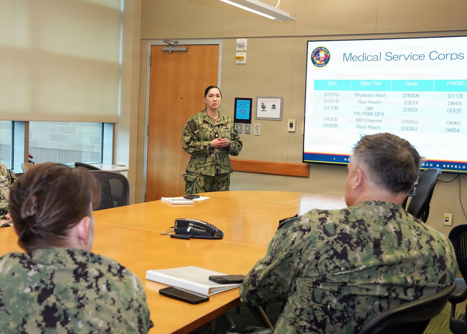 JOINT BASE SAN ANTONIO-FORT SAM HOUSTON – (March 4, 2026) – U.S. Navy Lt. Cmdr. Loreli Owens, director for Administration, Naval Medical Research Unit (NAMRU) San Antonio, briefs Capt. Kris Hodapp, deputy Corps Chief, Medical Service Corps (MSC) and Capt. Bryan Pyle, MSC Policy and Practice officer, during a visit to NAMRU San Antonio at the Battlefield Health and Trauma Research Institute (BHT). During the visit, Hodapp and Pyle toured research laboratories at BHT and the Tri-Service Research Laboratory and conducted independent record reviews with MSC officers. Additionally, they gave a State of the MSC briefing with emphasis on Navy Medicine’s North Star and Lines of Effort. Other areas of briefing included career progression, community values, manpower, promotion trends, and maintaining accuracy of military records. The MSC mission is to provide specialized healthcare, administrative, and scientific support to Naval forces, maximizing operational readiness and optimizing the "human weapon system". Comprised of professionals in clinical, scientific, and administrative fields, the MSC supports Navy Medicine’s mission to deliver manned, trained, and equipped medical units to the Fleet, Fleet Marine Force, and Joint Forces. NAMRU San Antonio, part of Navy Medicine Research & Development, conducts gap-driven combat casualty care, craniofacial, and directed energy research in support of Navy, Marine Corps and joint U.S. warfighter health readiness and lethality while engaged in routine and expeditionary operations. (Navy Photo by Burrell Parmer, NAMRU San Antonio Public Affairs/Released)