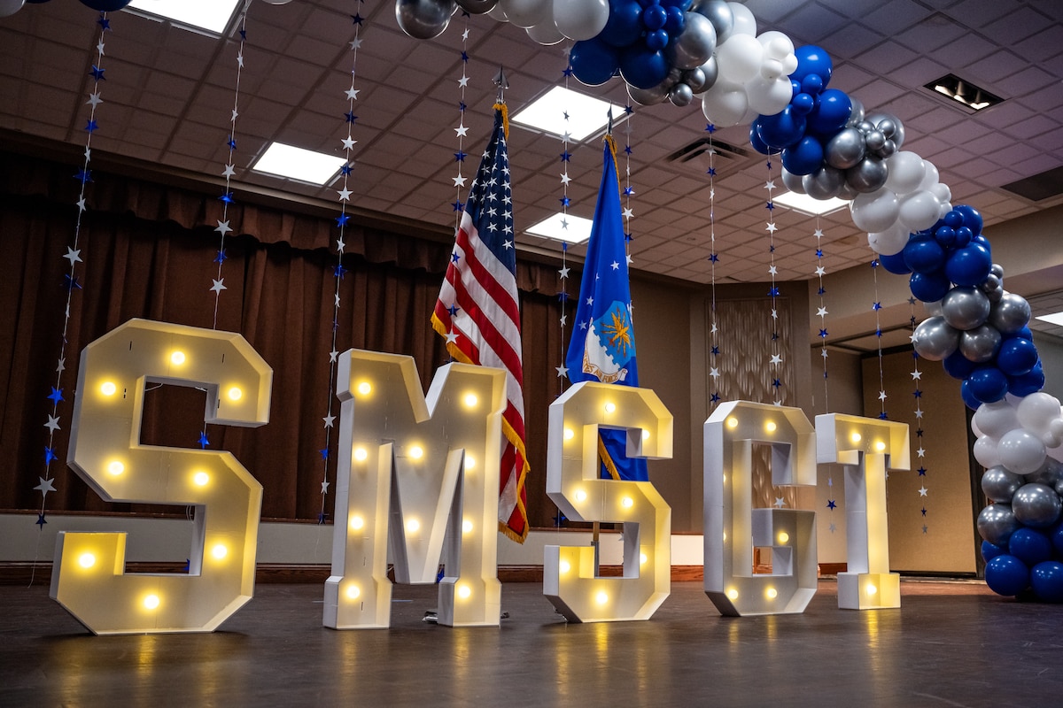 White letters "SMSGT", with yellow bulbs inside, stand under a blue and white balloon arch