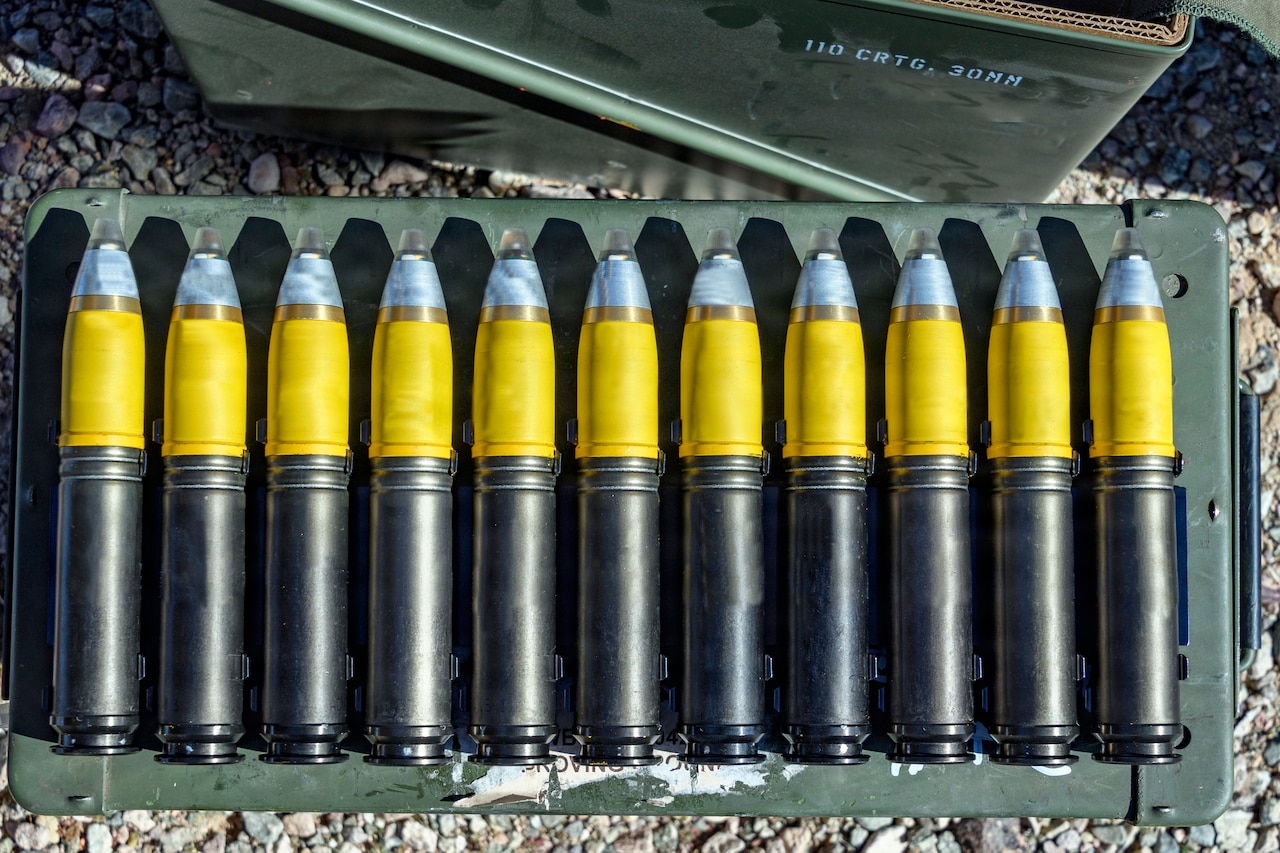 Eleven large munition rounds are lined up on a case outside.