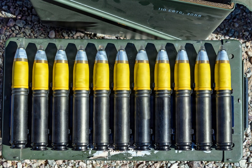 Eleven large munition rounds are lined up on a case outside.