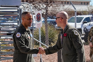 Two men in flight suits shake hands.