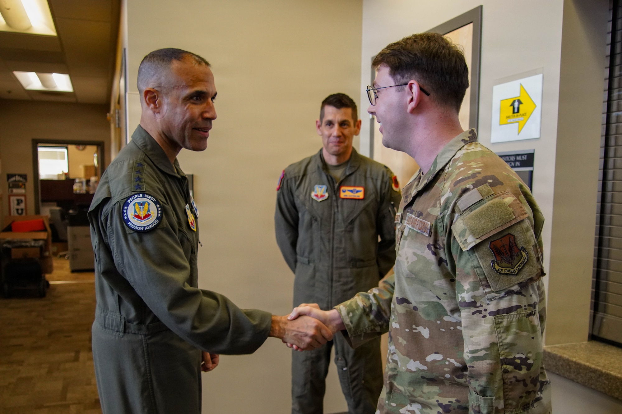 A man in a flight suit shakes hands with a man in a military uniform.