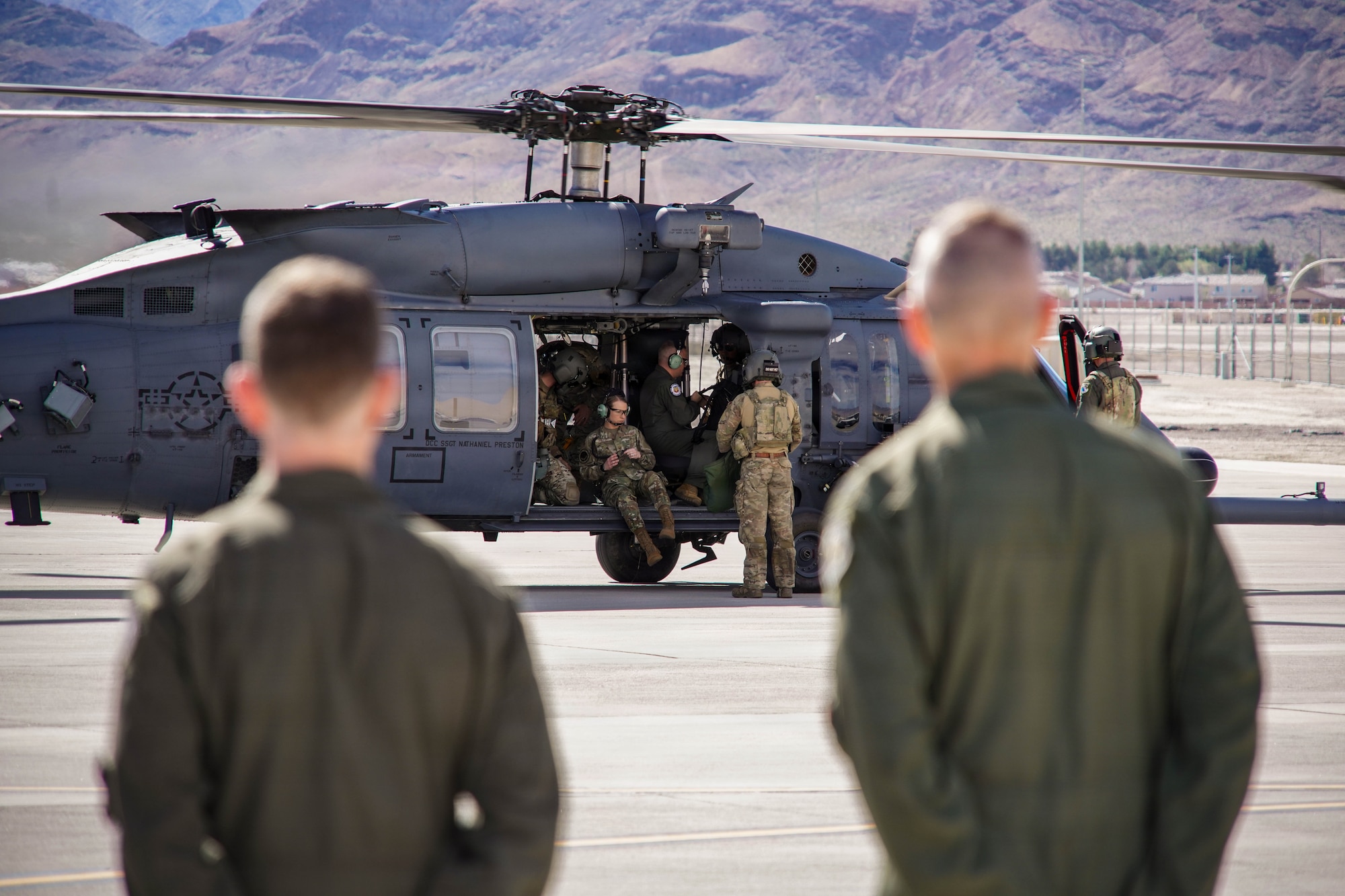 Two men in military uniforms look on as a man in a military uniform exits a helicopter.