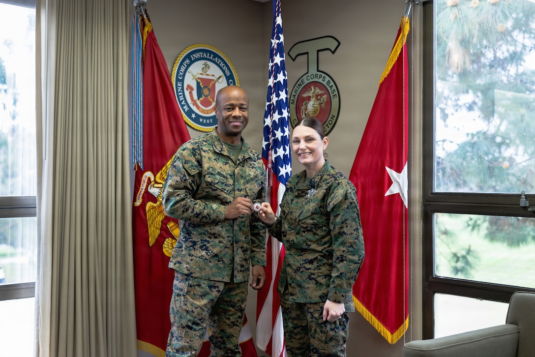 U.S. Marine Corps Brig. Gen. Brown, left, commanding general of Marine Corps Installations West, Marine Corps Base Camp Pendleton, presents a coin to U.S. Navy Petty Officer 1st Class  Coffey, a religious program specialist with MCIWEST and a California native, at MCB Camp Pendleton, Calif., Mar. 4, 2026. Coffey was recognized for being named Marine Corps Installations Command Sailor of the Year for fiscal year 2025. As the base’s lead petty officer and religious program specialist, Coffey mentored nine Sailors, six officers, one contract priest and one federal employee on all aspects of Professional Naval Chaplaincy and Sailorization in support of five subordinate commands across MCIWEST. (U.S. Marine Corps photo by Sgt. Rafael)