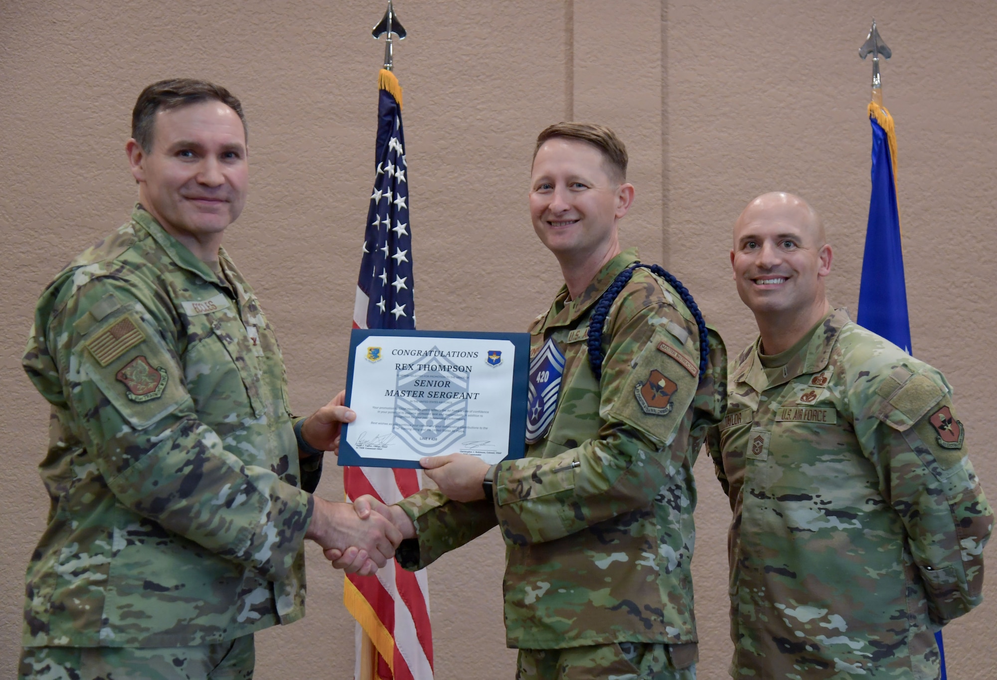 Three men in military uniforms pose for a group photo with the center man holding a certificate.