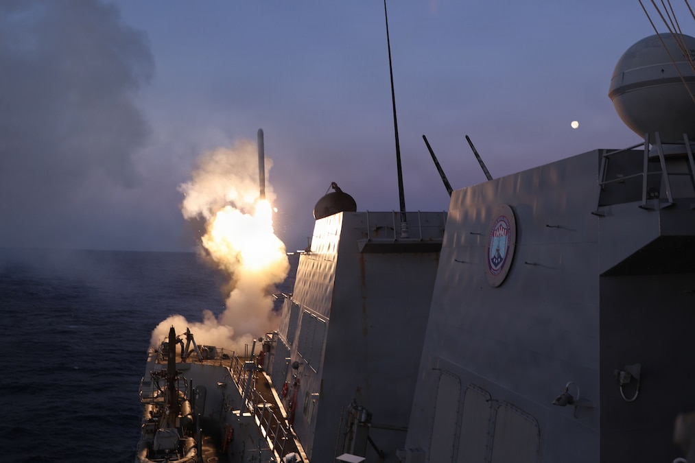 A ship at sea fires a missile, leaving behind a trail of smoke.