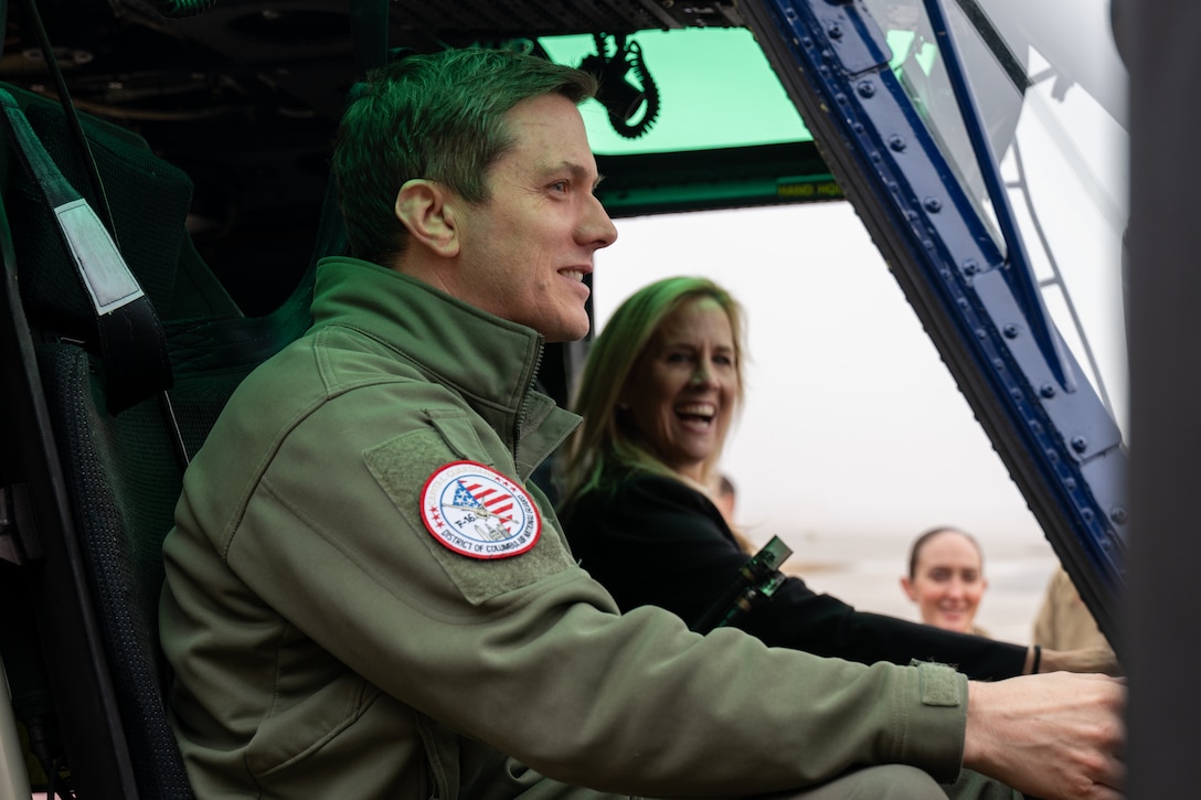 A man and a woman sit in the cockpit of a helicopter.