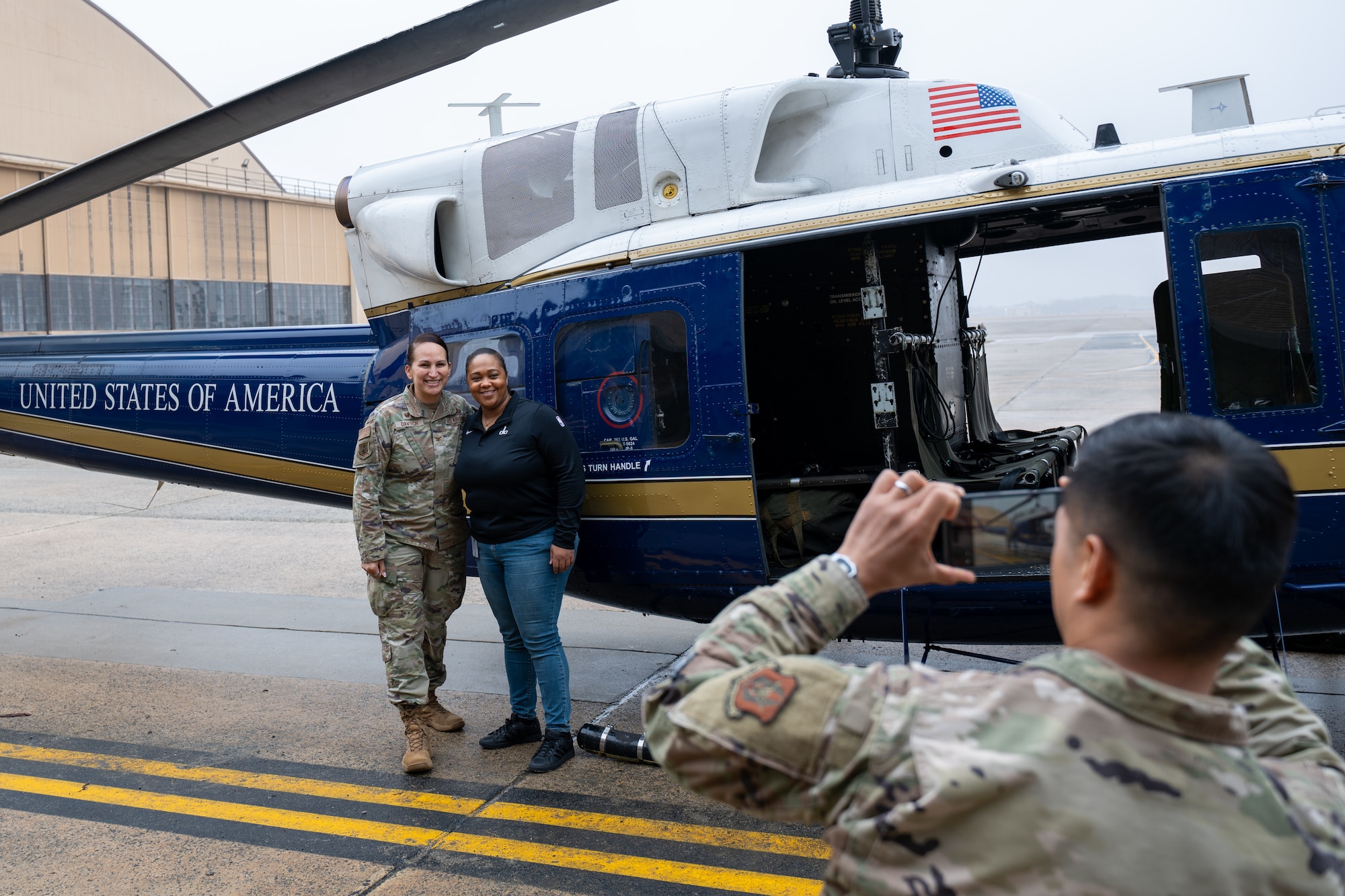 A man takes a photo of two women standing in front of a helicopter.