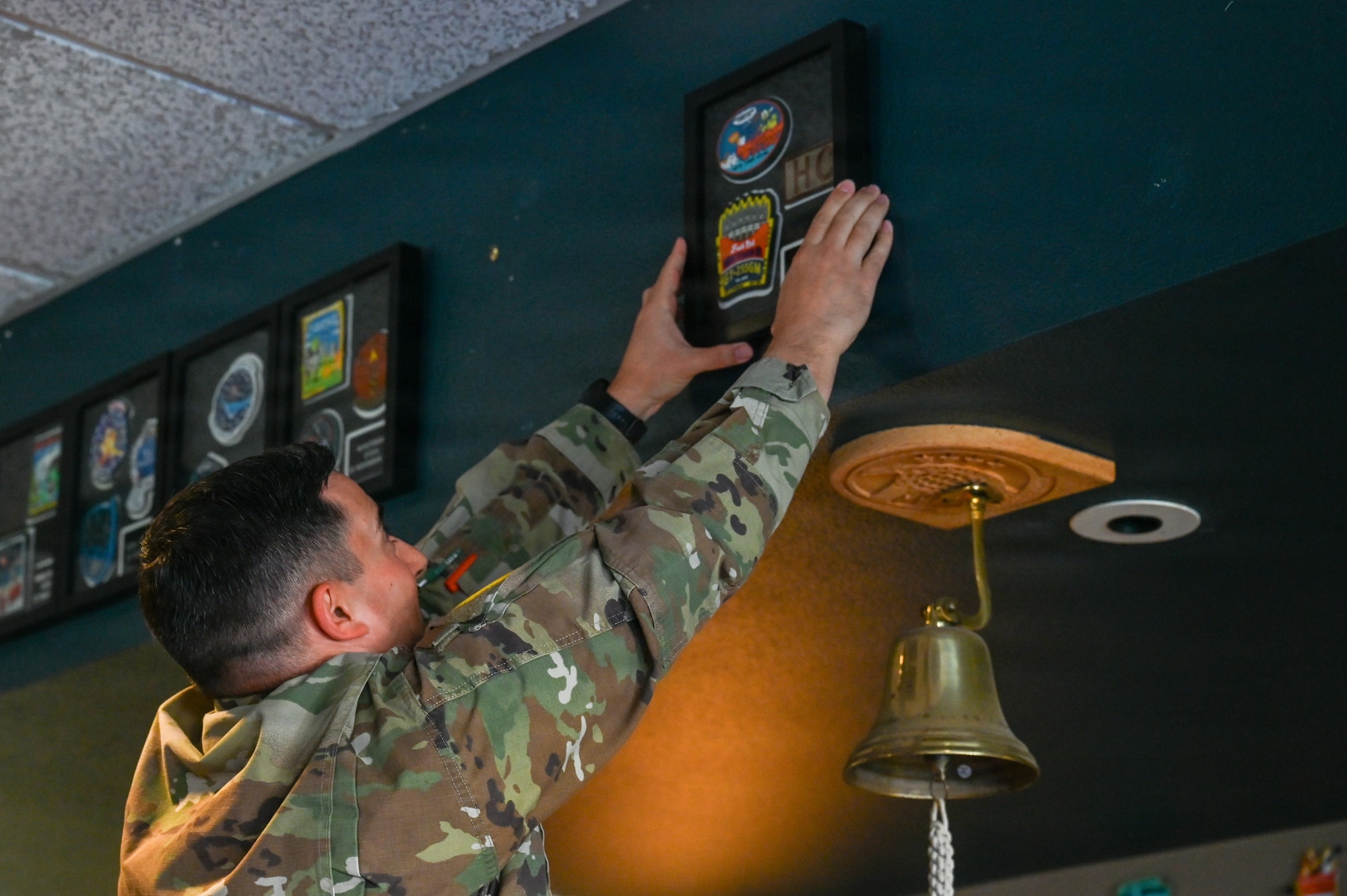 U.S. Space Force Lt. Col. Ralph Salazar, 2nd Range Operations Squadron commander, hangs a patch frame on the Pacific Coast Center heritage room wall.