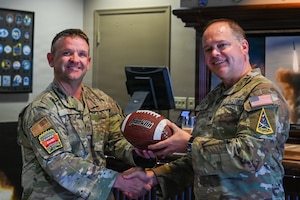 U.S. Space Force Col. James T. Horne III, Space Launch Delta 30 commander, hands the ceremonial game ball to U.S. Air Force Capt. Cecil Guy, Air Force Global Strike Command Intercontinental Ballistic Missile test manager. They both pose for a photo.