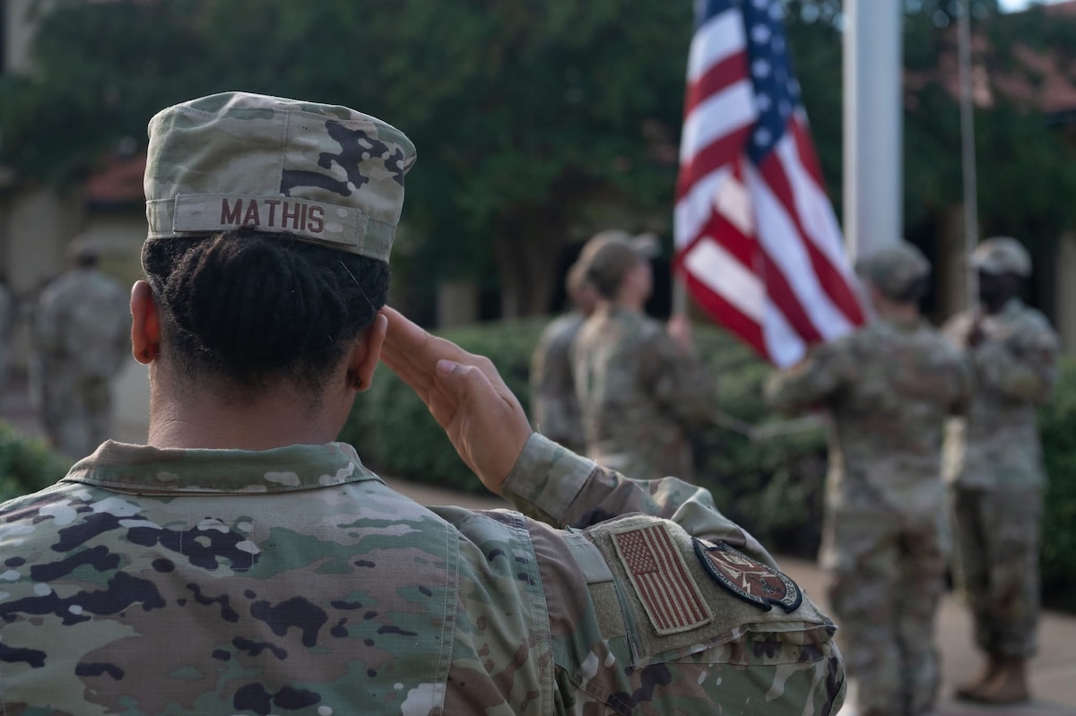 military member saluting an American flag while it is being lowered