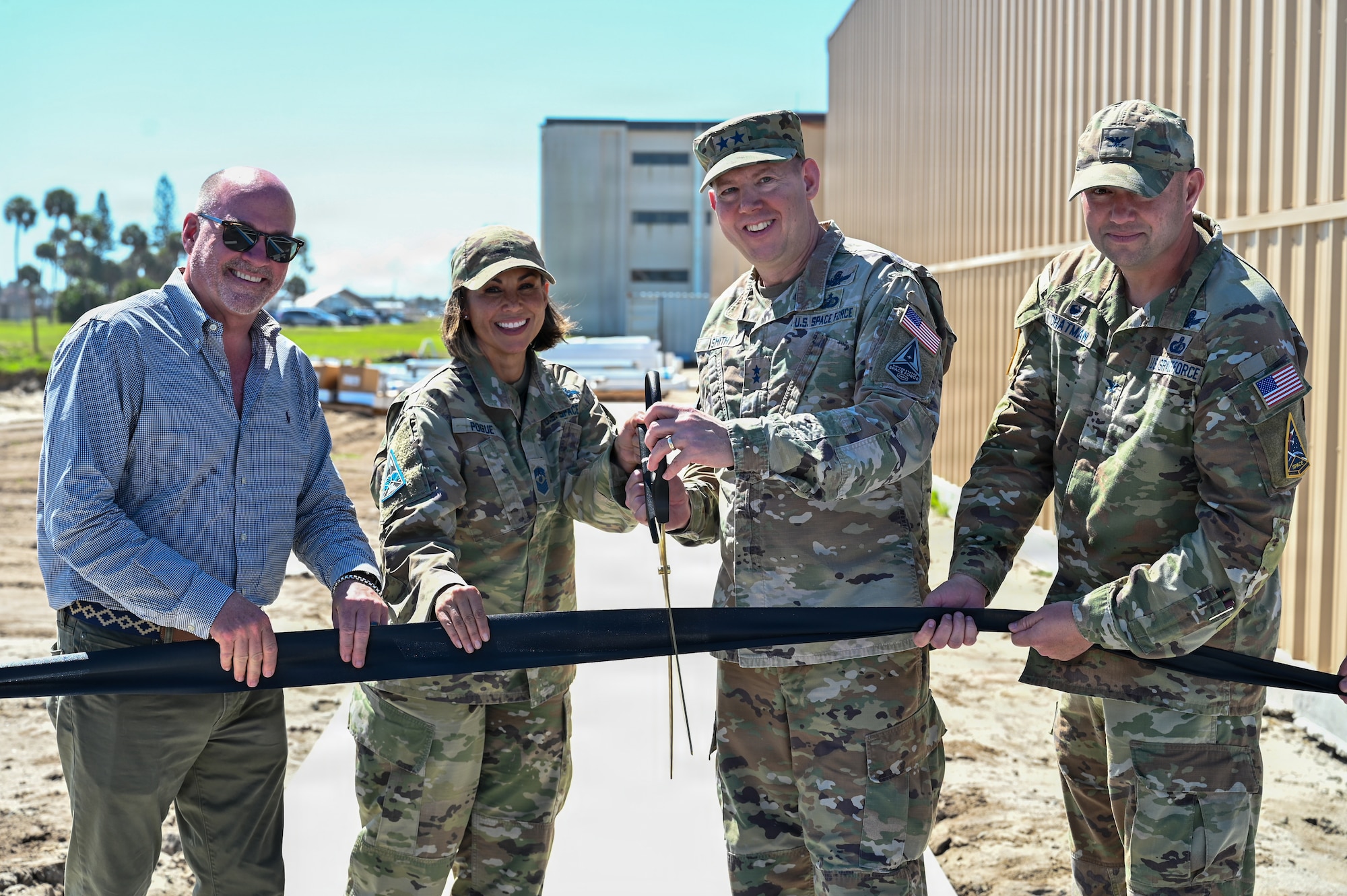 Four people holding ribbon and two with giant scissors posing for photo with construction in backgroung
