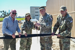 Four people holding ribbon and two with giant scissors posing for photo with construction in backgroung